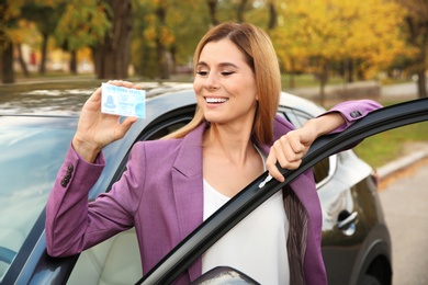 Woman holding driving license near open car