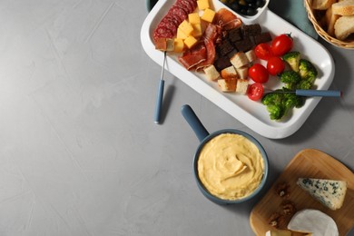 Photo of Fondue with tasty melted cheese, forks and different snacks on grey table, flat lay. Space for text