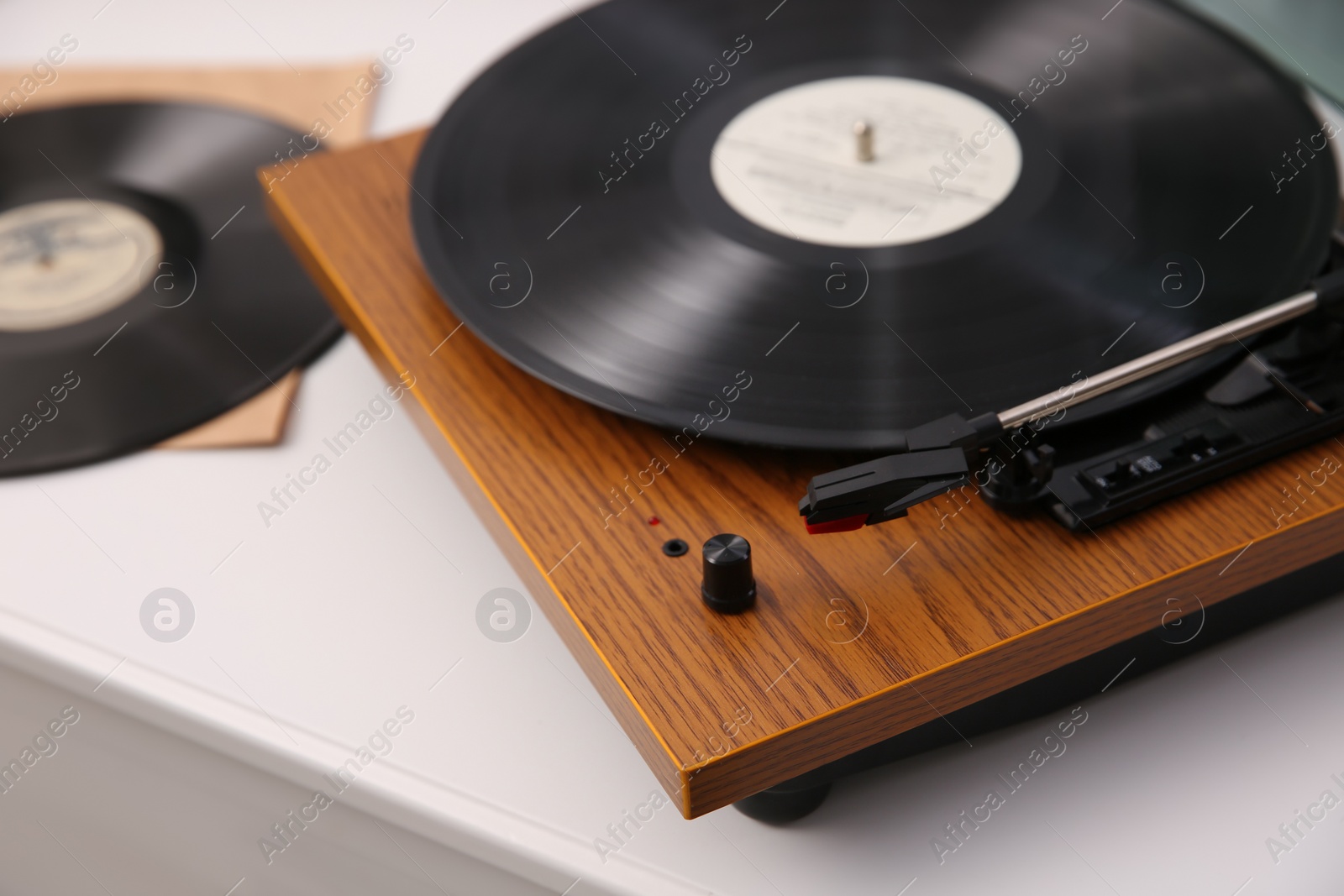 Photo of Stylish turntable with vinyl record on white chest of drawers, closeup