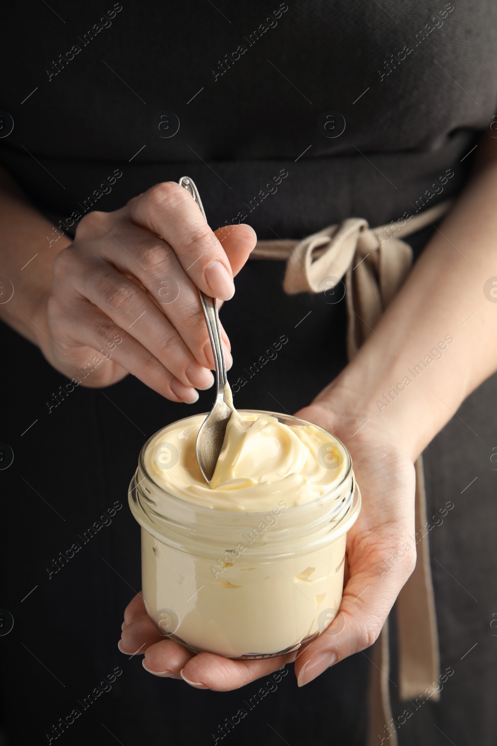 Photo of Woman holding spoon and jar of delicious mayonnaise, closeup