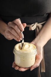 Photo of Woman holding spoon and jar of delicious mayonnaise, closeup