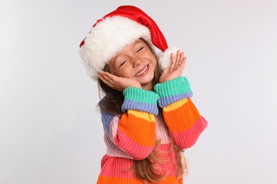 Photo of Happy little child in Santa hat on light grey background. Christmas celebration