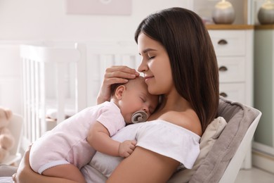 Happy young mother with her sleeping baby in armchair at home