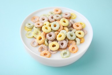 Photo of Tasty colorful cereal rings and milk in bowl on turquoise background