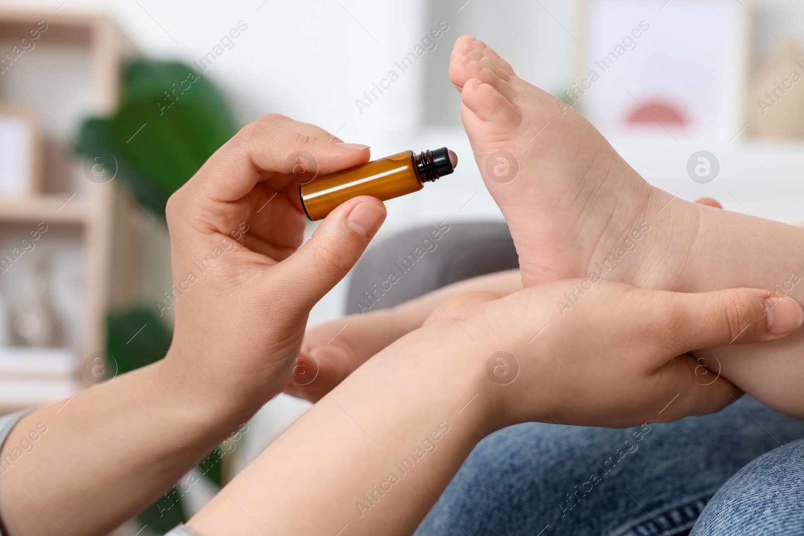 Photo of Mother applying essential oil from roller bottle onto her baby`s heel indoors, closeup