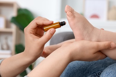 Mother applying essential oil from roller bottle onto her baby`s heel indoors, closeup