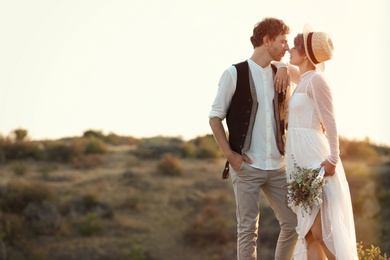 Photo of Happy newlyweds with beautiful field bouquet standing on rock outdoors