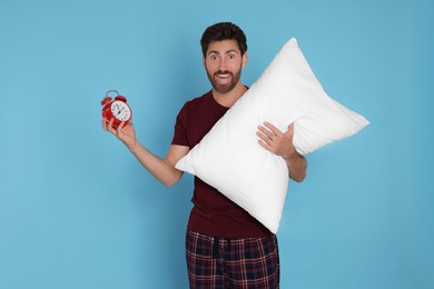 Photo of Emotional overslept man with alarm clock and pillow on light blue background
