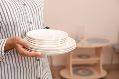 Photo of Woman holding stack of clean dishes in kitchen, closeup. Space for text