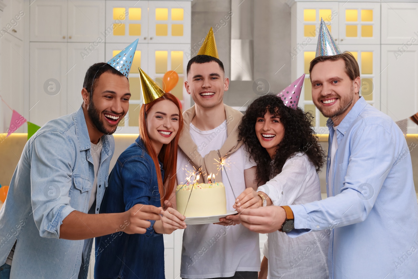 Photo of Happy friends with tasty cake and sparklers celebrating birthday in kitchen