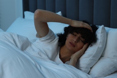 Photo of Young woman suffering from headache in bed at night