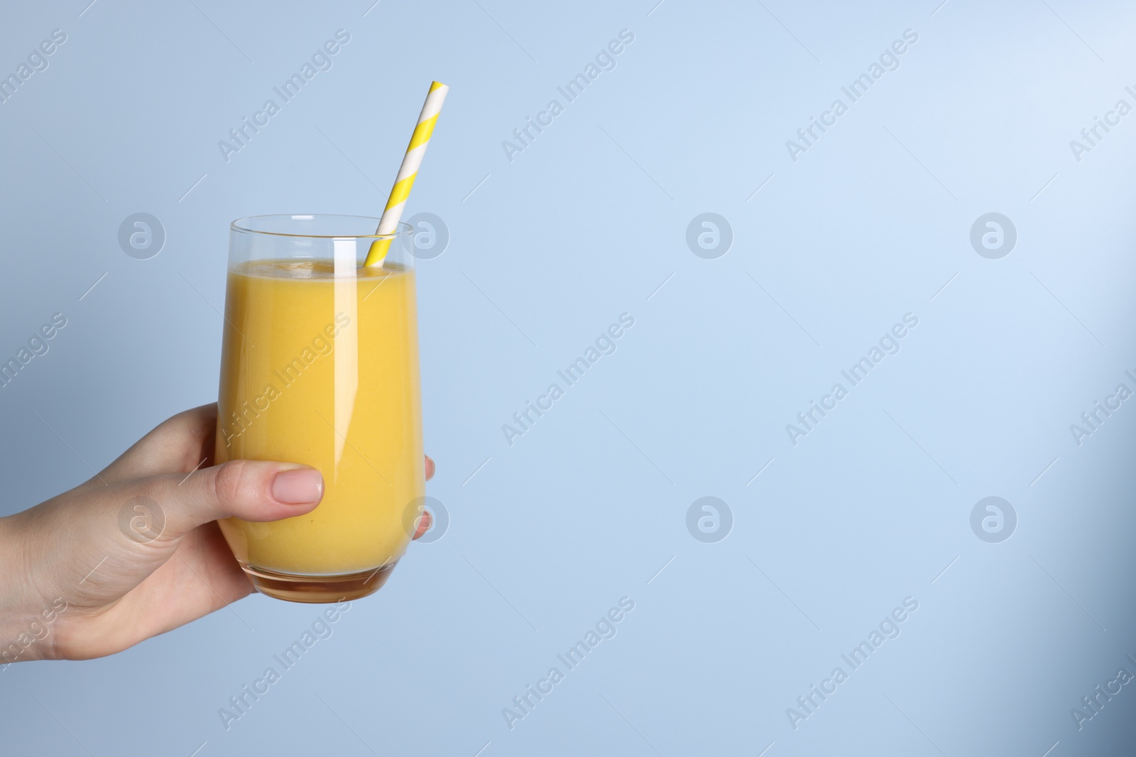 Photo of Woman holding glass of tasty smoothie on light blue background, closeup. Space for text