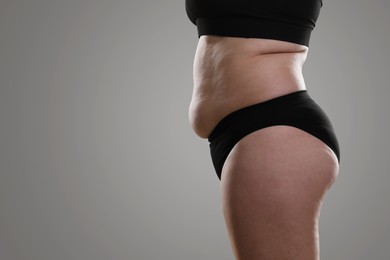 Woman with excessive belly fat on grey background, closeup. Overweight problem