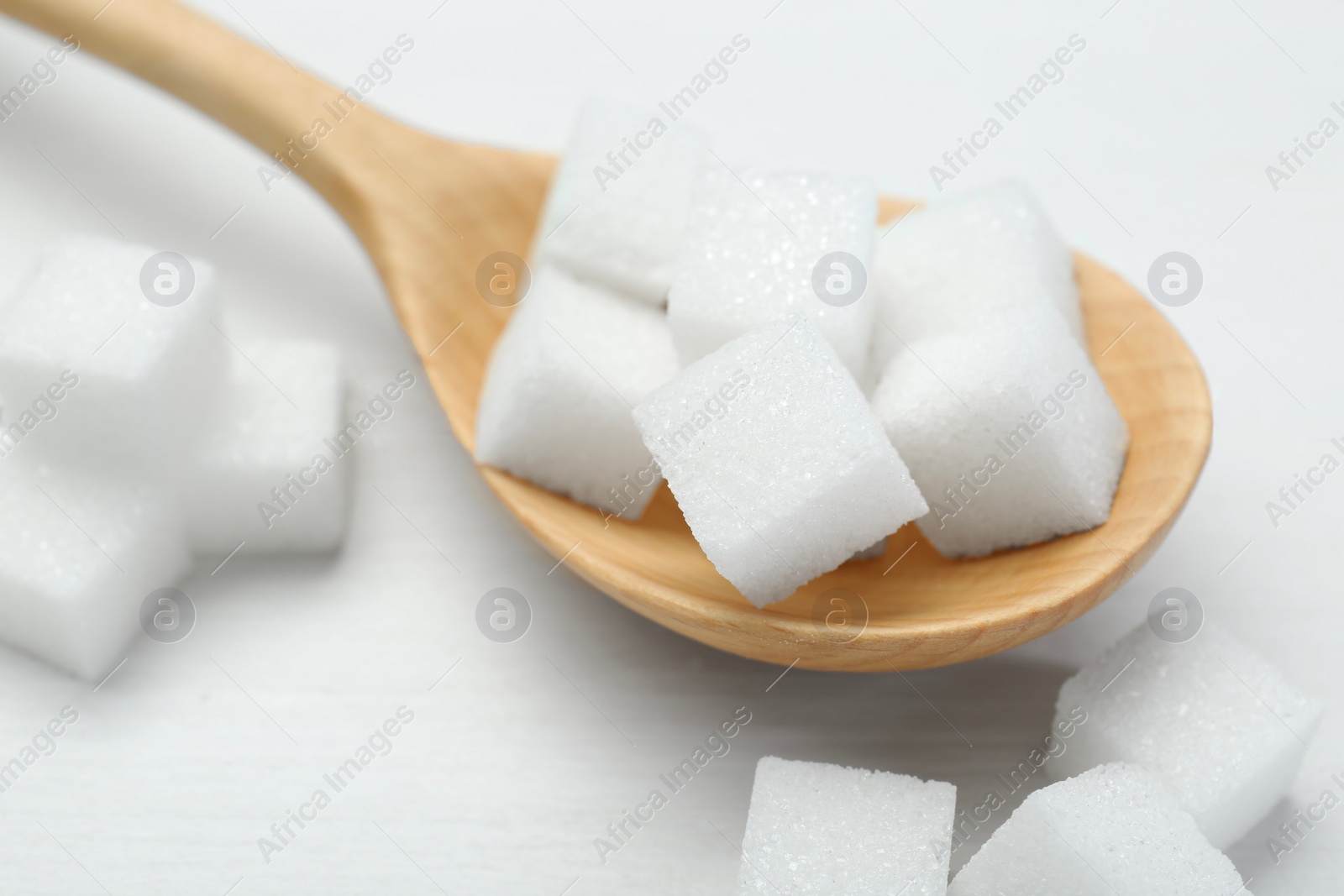 Photo of Many sugar cubes and wooden spoon on white table, closeup