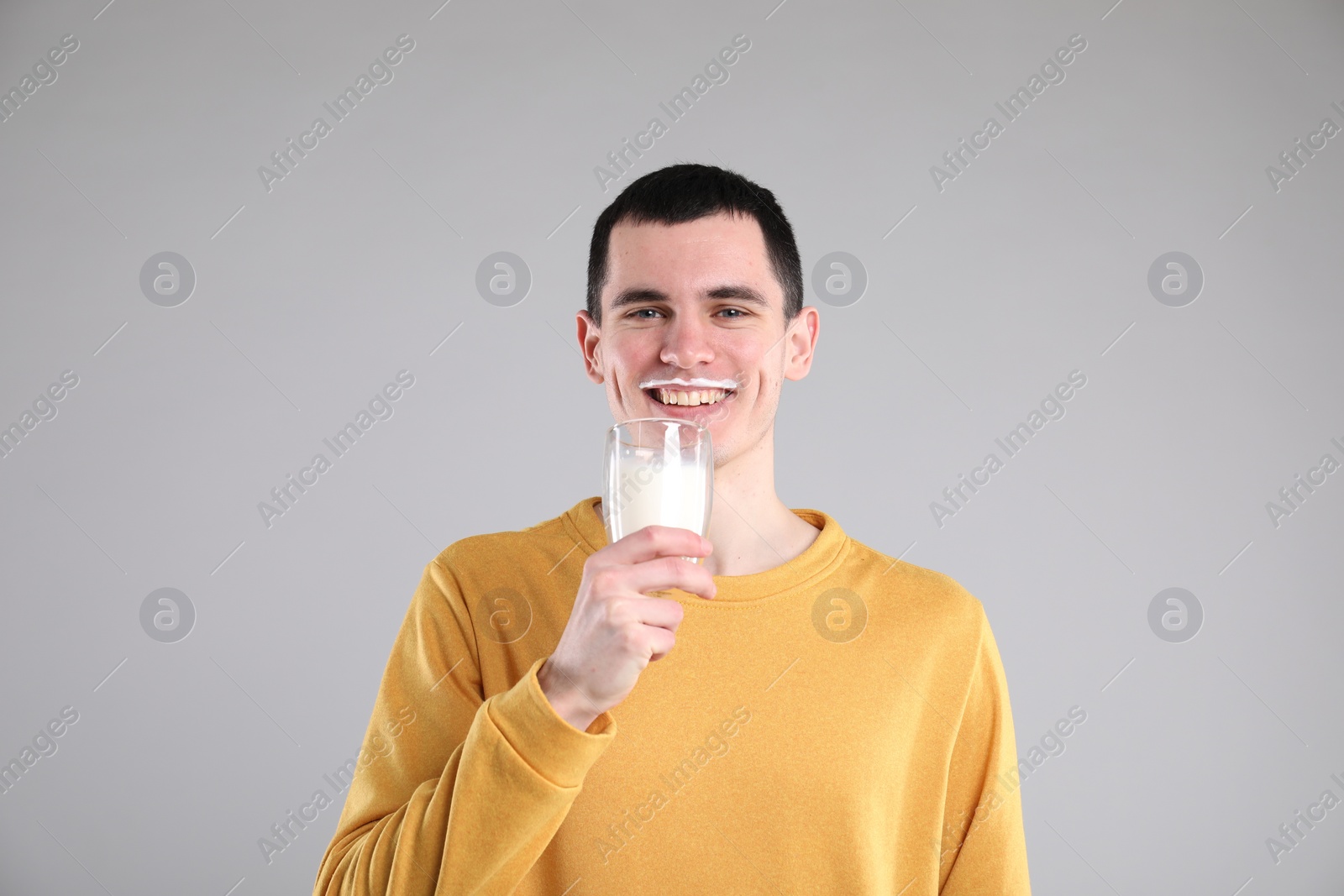 Photo of Happy man with milk mustache holding glass of tasty dairy drink on gray background