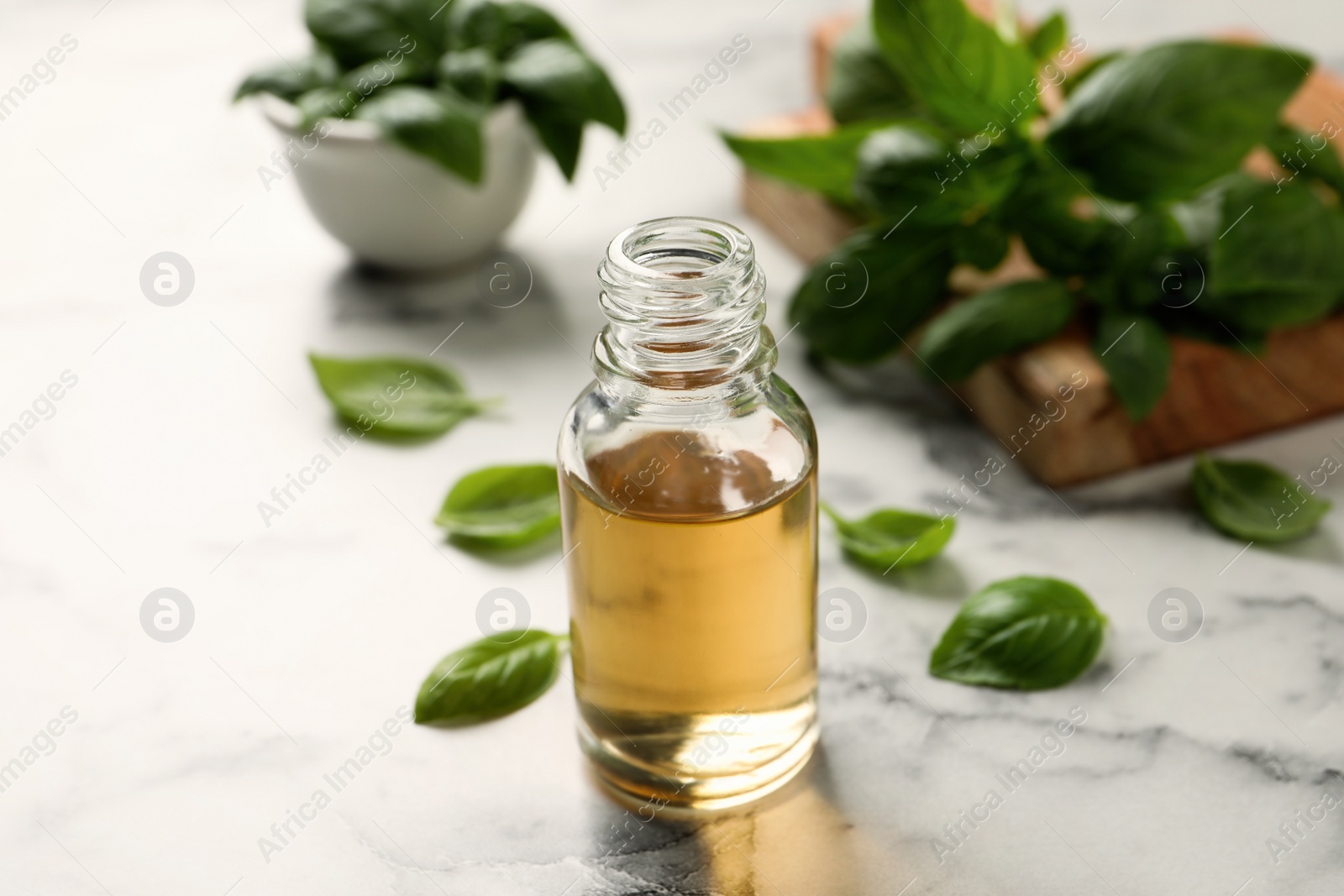 Photo of Glass bottle of basil essential oil and leaves on white  marble table