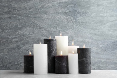 Photo of Set of burning candles on table against grey marble background