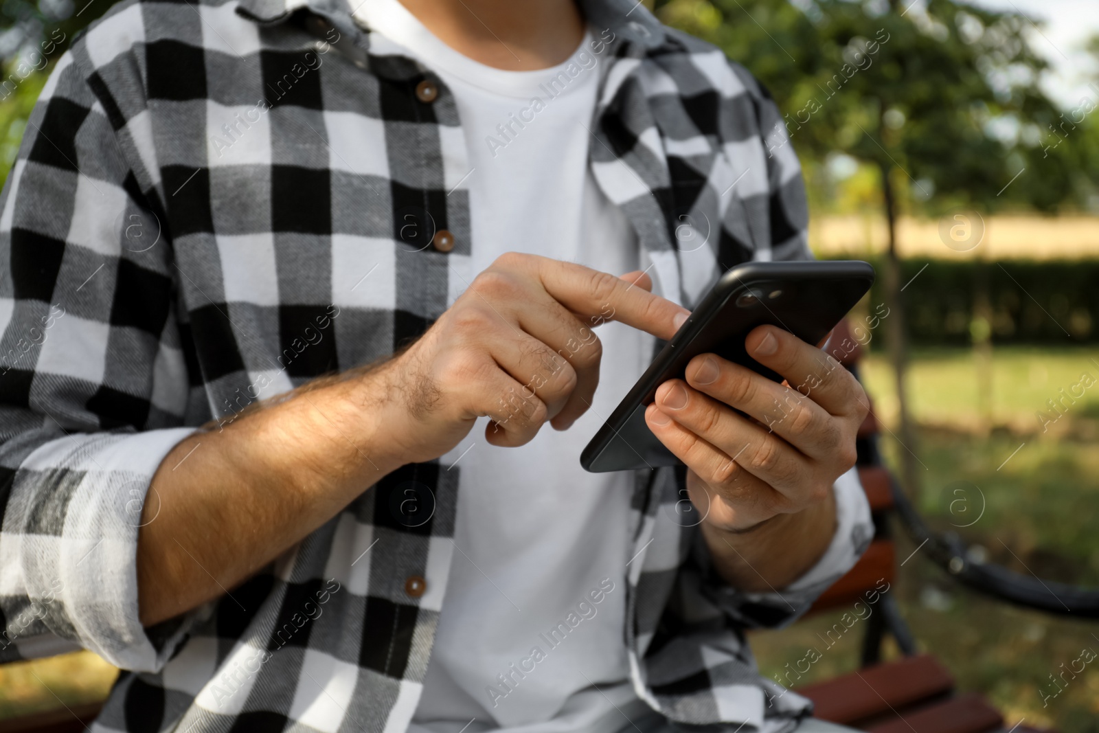 Photo of Young man with smartphone in park on summer day, closeup