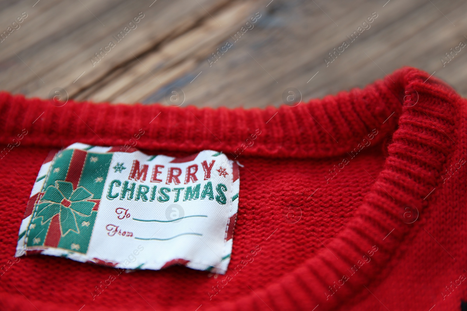 Photo of Christmas sweater with tag on wooden background, closeup