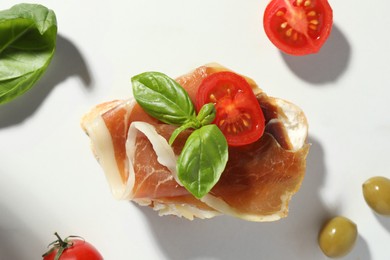 Photo of Tasty sandwich with cured ham, basil and tomato on white marble table, flat lay