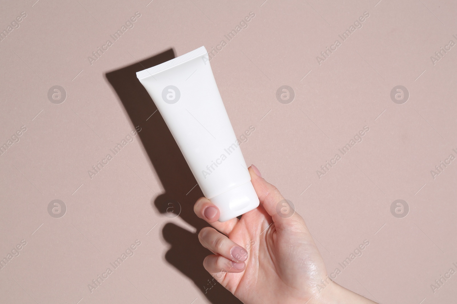 Photo of Woman with tube of cream on beige background, closeup