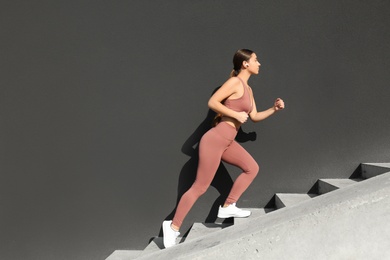 Photo of Young woman in stylish sports wear running along stone stairs. Space for text