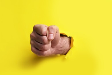 Photo of Man breaking through yellow paper with fist, closeup