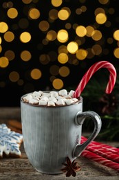 Delicious hot chocolate with marshmallows and candy cane on wooden table against blurred lights