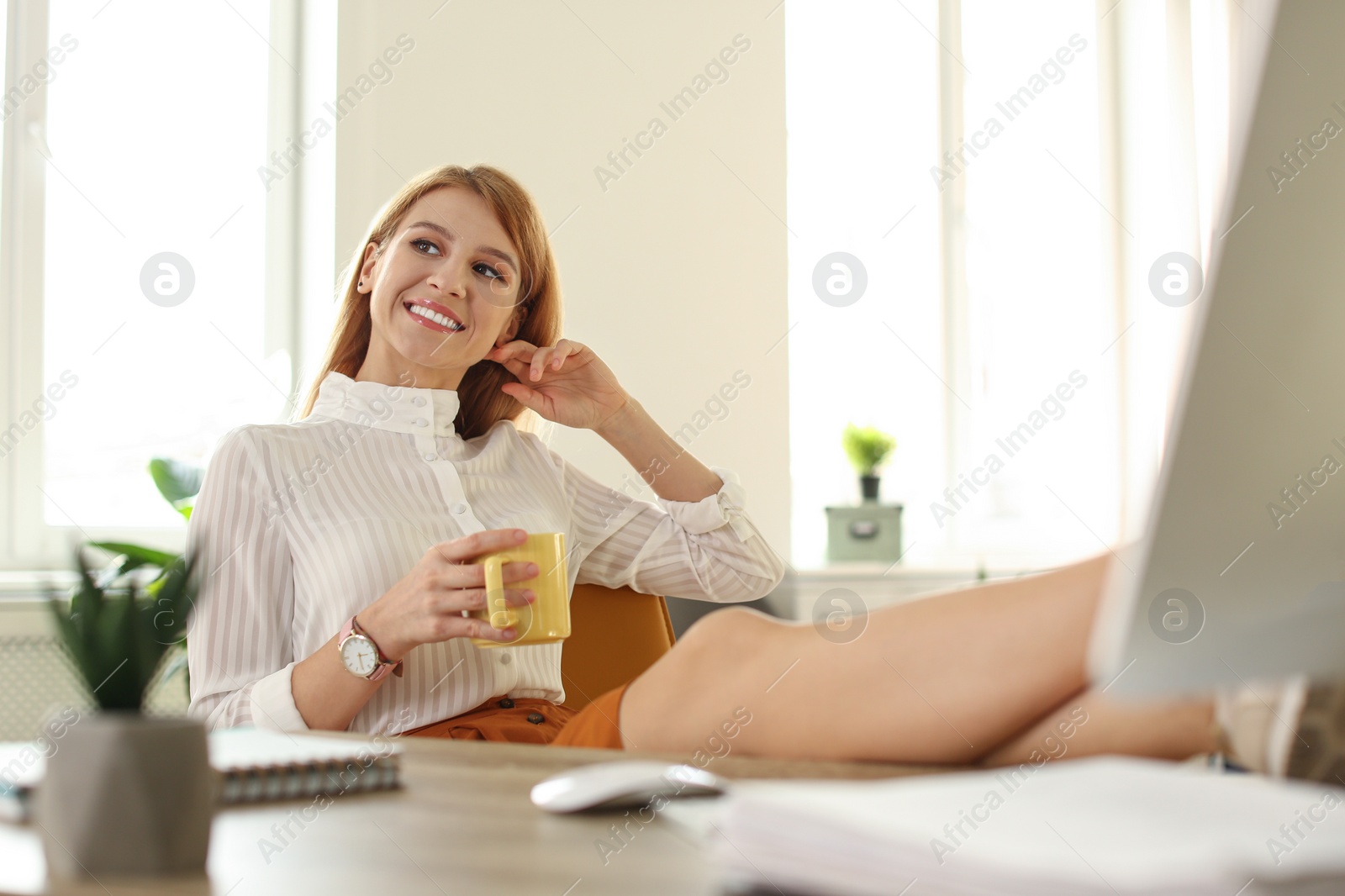 Photo of Young woman with cup of drink relaxing at table in office during break