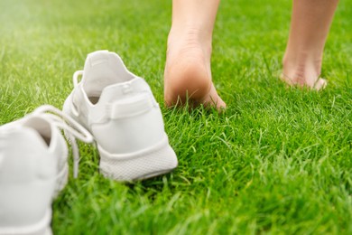 Photo of Woman leaving her sneakers and walking away barefoot on green grass, closeup