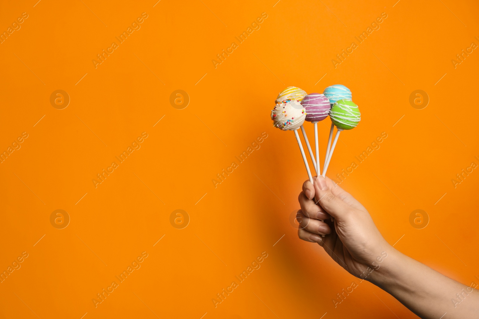 Photo of Woman holding bright delicious cake pops on color background, closeup. Space for text