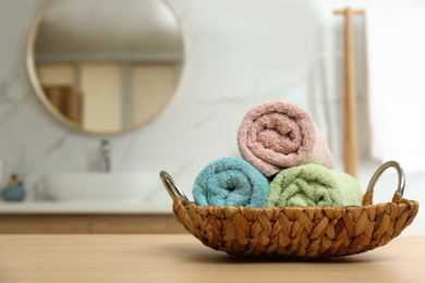 Photo of Rolled color towels on wooden table in bathroom. Space for text