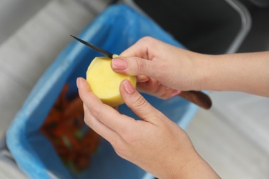 Woman peeling fresh potato with knife near garbage bin, above view