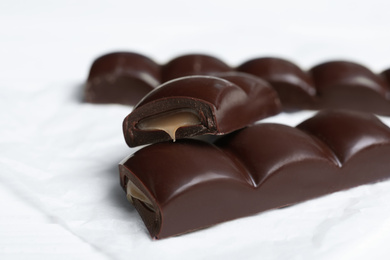 Photo of Pieces of chocolate with caramel filling on white table, closeup