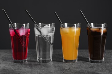 Glasses of different refreshing soda water with ice cubes and straws on grey table