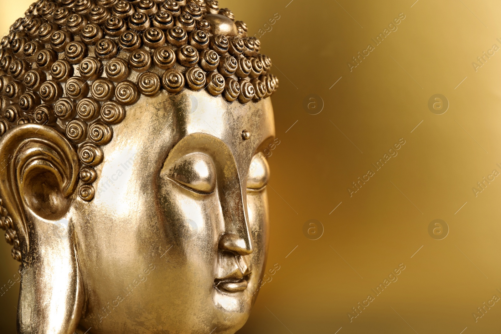 Photo of Buddha statue on golden background, closeup. Space for text