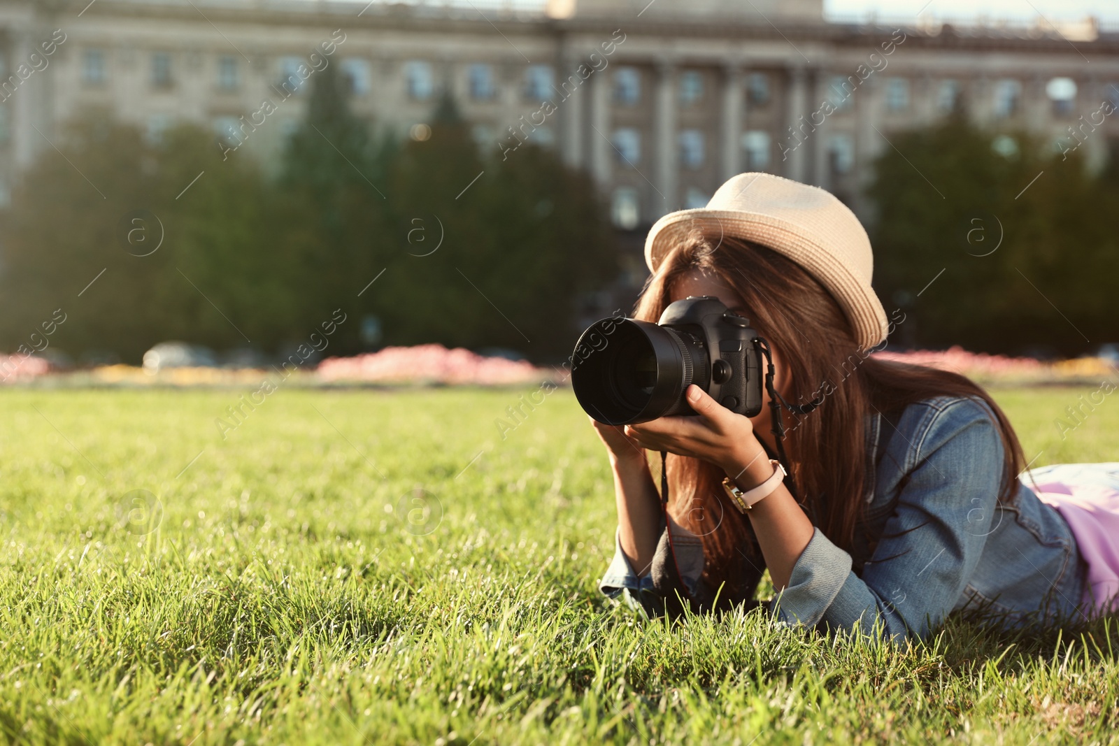Photo of Young female photographer taking photo with professional camera on grass outdoors. Space for text