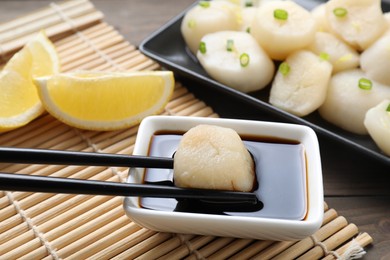 Photo of Taking raw scallop from bowl of soy sauce with chopsticks at wooden table, closeup