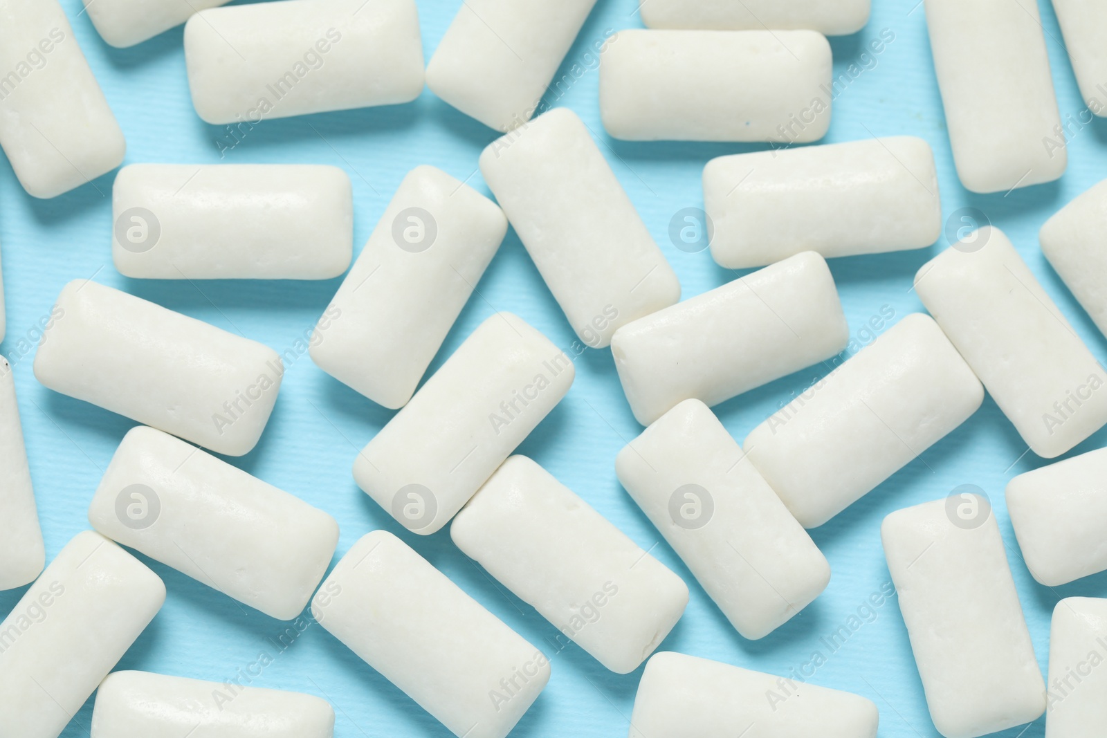 Photo of Tasty white chewing gums on light blue background, flat lay