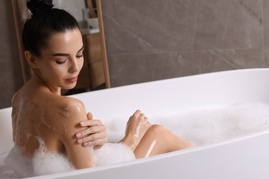 Woman taking bath with shower gel indoors