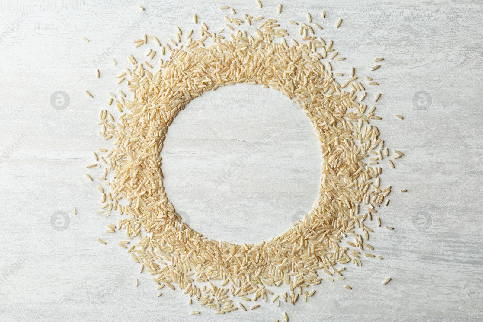 Photo of Round frame made with brown rice on white wooden background, top view. Space for text