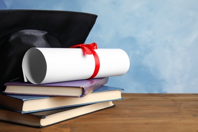 Graduation hat, books and student's diploma on wooden table against light blue background