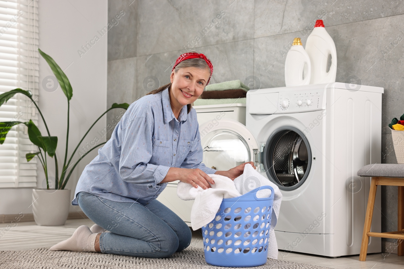 Photo of Happy housewife with laundry basket near washing machine at home