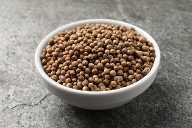 Photo of Dried coriander seeds in bowl on gray textured table, closeup