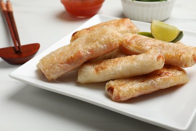 Photo of Tasty fried spring rolls, lime and sauces served on white marble table, closeup