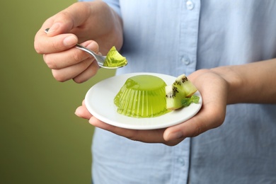 Photo of Young woman eating tasty kiwi jelly on green background, closeup