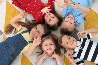 Photo of Adorable little children lying on bright carpet together in kindergarten, top view. Playtime activities