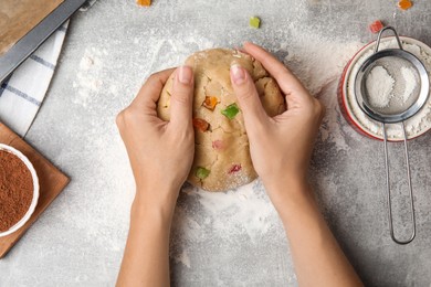 Photo of Woman holding unbaked cookie with candied fruits at grey table, top view