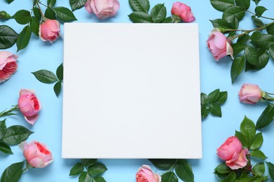 Photo of Blank canvas and beautiful pink roses on light blue background, flat lay. Space for design