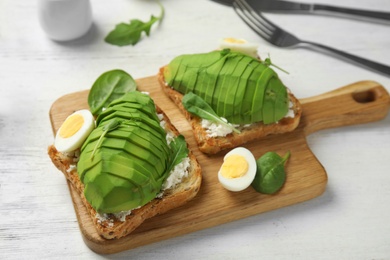 Tasty toasts with avocado and quail egg served on white wooden table